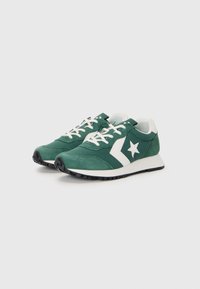 Zapatillas verdes con parte superior de ante y malla, logo de estrella blanca, cordones blancos y suela de goma negra. Diseño retro elegante, de perfil bajo.