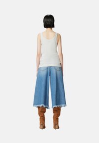 Top grigio chiaro, culotte di jeans blu larghi con orlo sfrangiato e alti stivali in suede marroni con tacco alto. Visto da dietro.