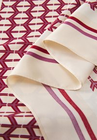 Tissu à motifs présentant un design géométrique en rouge et crème, avec une texture lisse et des rayures diagonales dans diverses nuances de rouge et de rose.