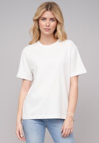 T-shirt en coton blanc à manches courtes, col rond et coupe décontractée, associé à un jean bleu clair. Texture lisse, sans motifs visibles.