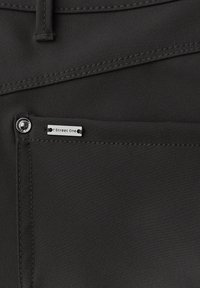 Zbliżenie na czarną kieszeń z tkaniny z metalowym nitem i metką "Street One" nad podwójnymi przeszyciami szwów.