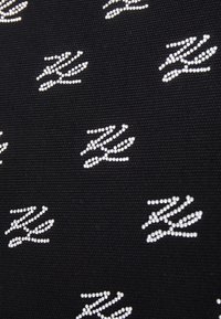 Černá látka se vzorem malých bílých rukou, zdobených stříbrnými drahokamy, vytvářející texturovaný vizuální efekt.