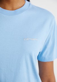 T-shirt di cotone azzurro con collo a girocollo rigato e logo "carhartt" ricamato in bianco sulla parte sinistra del petto.