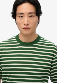 Camiseta de manga corta a rayas verdes y crema con cuello redondo y una textura suave. Las rayas están espaciadas uniformemente y son consistentes en ancho.