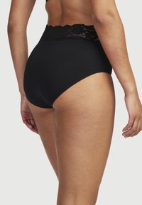 Korkeavyötäröiset mustat alushousut, joissa on kukkakuvioitu pitsivyötärö, pehmeä kangas, sileä pinta ja koristeelliset aaltoilevat reunat.