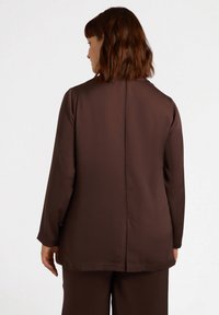 Brązowa bluzka z długim rękawem o gładkiej fakturze, z prostym krojem, detalem na szwie z tyłu oraz luźnym krojem dla komfortu.