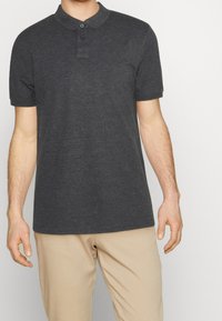 Polo noir en tissu avec une texture douce. Doté d'un col, d'une patte de boutonnage à trois boutons et de manches courtes.