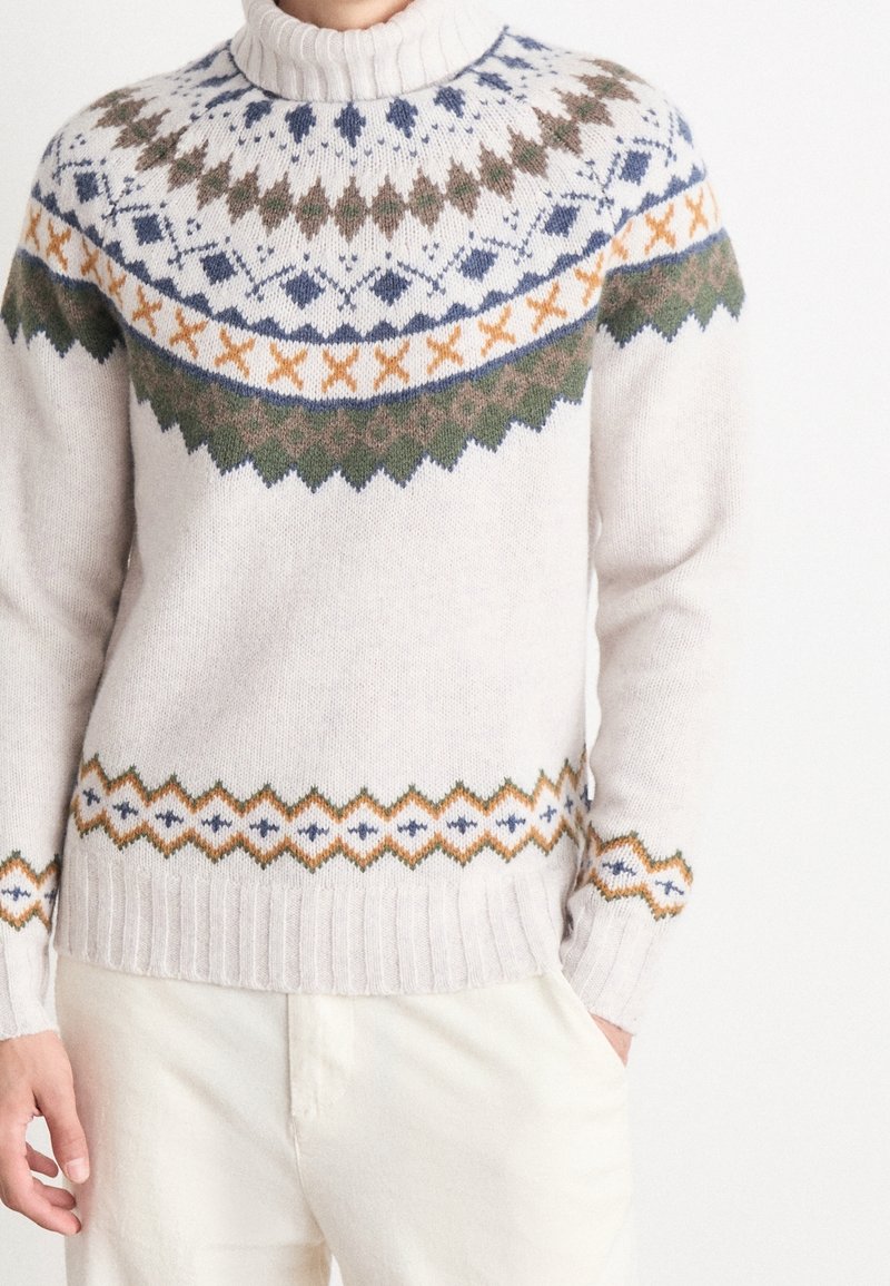 Sweter dziany w jasnym beżu z wysokim kołnierzem. Ma geometryczne wzory w ciemnej zieleni, niebieskim, pomarańczowym i brązowym wokół karczku. Żebrowany dół.