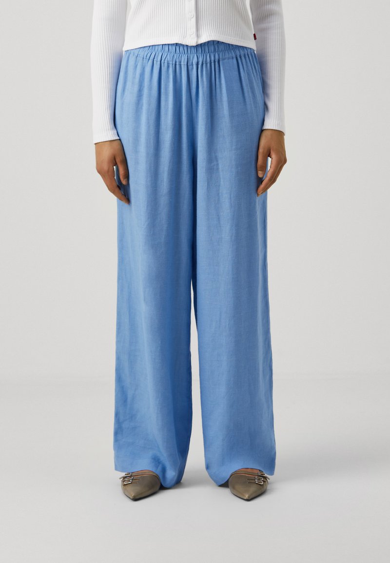 Pantalons larges bleu clair avec une taille élastique et une texture en lin doux, associés à des chaussures plates à bout pointu dans une teinte douce.