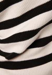 Gros plan d'un tissu en maille côtelée avec des rayures horizontales larges noires et blanches alternées, montrant la texture et les plis.