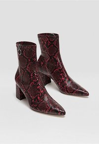 Bottines en cuir imprimé peau de serpent rouge et noir, avec un bout pointu et un talon épais. Fermeture éclair latérale pour un enfilage facile avec une finition texturée.
