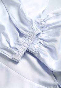 Biely textil s hladkou textúrou, ktorý obsahuje z gatherované elastické detaily na švoch. Dizajn zahŕňa jemné záhyby a nepretržité línie.
