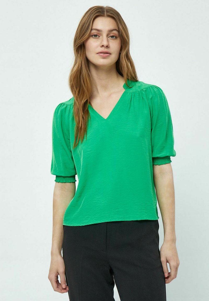 Top verde a V con maniche corte a sbuffo, realizzato in tessuto testurizzato e con una vestibilità rilassata. Abbinato a pantaloni neri per creare contrasto.