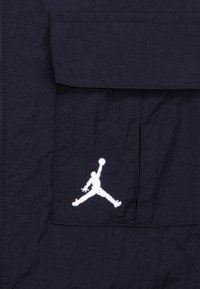 Giacca navy con tessuto strutturato, una tasca a pattina ben visibile e il logo Air Jordan bianco ricamato sul davanti.
