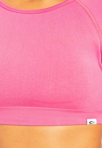 Close-up van een roze geribbelde sportbeha gedragen op een gebruinde torso, met zichtbare textuur van de stof en een klein wit label aan de zijkant.