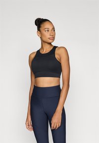 Μαύρο αθλητικό σουτιέν με στρογγυλεμένο ντεκολτέ και φαρδιές τιράντες, κατασκευασμένο από λείο ύφασμα, σε συνδυασμό με ναυτικά ψηλόμεσα κολάν με υφασματικά διακοσμητικά στοιχεία.