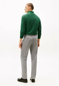 Pull en maille verte avec un col, associé à un pantalon gris clair avec des poches arrière et une coupe slim. Des chaussures noires complètent la tenue.