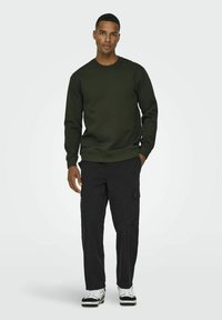Olive green sweatshirt with a round neck and ribbed cuffs, paired with black cargo pants featuring side pockets and black-and-white sneakers.