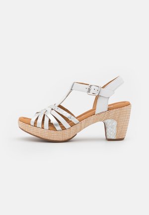 Hvid læder sandal med hæl og spænde, flettet platformsål og sølvfarvede teksturerede accenter på stropper og hældetalje.