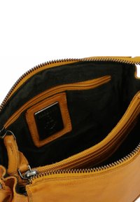 L'interno della borsa di pelle gialla presenta una fodera nera con compartimenti con cerniera e un'etichetta del marchio. Texture liscia con dettagli di cucitura visibili.