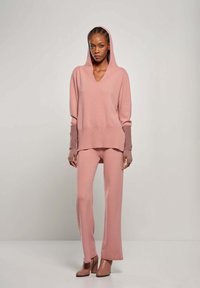 Pullover rosa a maglia con cappuccio e scollatura a V, abbinato a pantaloni ampi coordinati. Tessuto texture con dettagli a contrasto sui polsini.