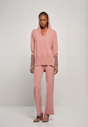 Roze gebreide pullover met capuchon en V-hals, gecombineerd met bijpassende wijde broek. Textuurstof met contrasterende details op de manchetten.