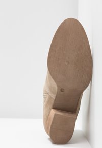 Beżowe zamszowe buty na słupku, z teksturowaną podeszwą i gładkim wykończeniem cholewki. Rozmiar oznaczony jako 37.