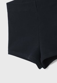 Gros plan sur un short en tissu côtelé noir montrant les détails de l'ourlet et de la couture latérale sur un fond clair.
