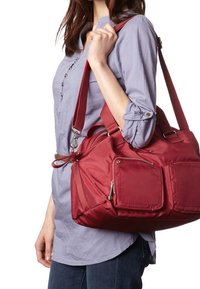 Punainen nailonista valmistettu käsilaukku, jossa on kaksinkertaiset vetoketjulliset taskut, tukeva olkahihna ja pehmeä tekstuuri, käytetty olalla vaaleanharmaan paidan kanssa.