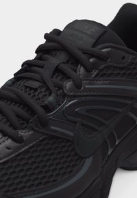 Κοντινό πλάνο μαύρου αθλητικού παπουτσιού Nike M2K Tekno με δίχτυ, επενδύσεις δέρματος, χοντρές κορδονόσχοινες και ορατό λογότυπο Nike στη πλευρά.