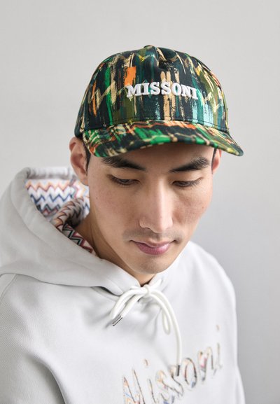 La casquette présente un design abstrait coloré avec des teintes de vert, d'orange et de jaune. L'avant porte "MISSONI" en broderie blanche. Matériau en coton.