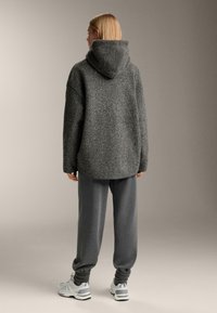 Sivi puhasti pulover s kapuco z ohlapnim krojem, kombiniran s sivimi trenirkami in belimi supergami. Mehka tekstura in velika zasnova.