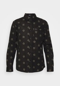 Chemise noire à manches longues avec de petits motifs beige paisley et une poche poitrine avec un petit logo blanc "Volcom".
