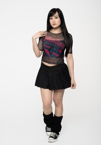 Transparent black mesh t-shirt featuring red "Judas Priest" graphic, paired with a black pleated mini skirt, and black leg warmers.