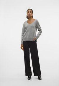 Pull gris à col V avec une coupe décontractée, associé à un pantalon large noir et des chaussures à talons noires. Texture lisse et détails minimalistes.