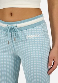 Gaiši zilas sporta bikses ar rūtainu rakstu, riboto faktūru un baltām detaļām. Aprīkotas ar aukliņu jostasvietā un izšūtu logotipu.