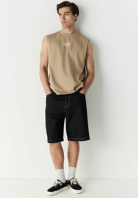 T-shirt sans manches beige avec le texte "Copenhague", associé à un short en denim noir, des chaussettes blanches à la cheville et des baskets en toile noires.