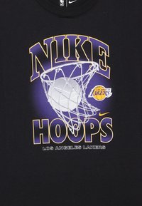 Tecido preto com o texto Nike Hoops, uma bola de basquete entrando numa cesta, e o logótipo dos Los Angeles Lakers em roxo e amarelo.
