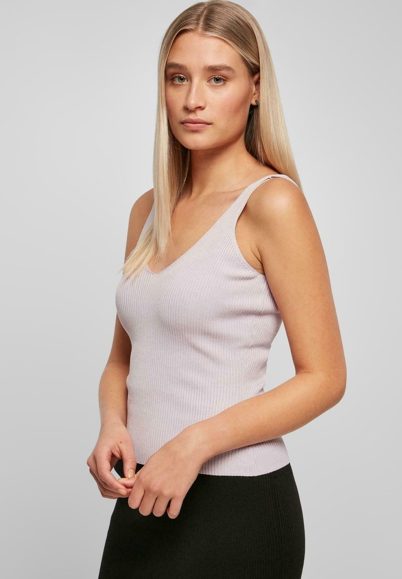 Licht paarse geribde tanktop met een v-hals en dunne bandjes, gecombineerd met een zwart aansluitend rokje dat gestructureerde patronen toont.