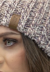 Knitted beanie in cream and purple tones, featuring a textured pattern and a brown leather tag with the brand name.