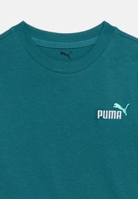 Τιρκουάζ μπλουζάκι με στρογγυλή λαιμόκοψη και μικρό λευκό και γαλάζιο λογότυπο Puma στο αριστερό στήθος, καθώς και μαύρο λογότυπο Puma μέσα στη λαιμόκοψη.