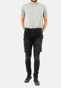 Šedé tričko s krátkým rukávem a logem, černé distressed cargo džíny s roztrhanými koleny a černé tenisky. Jednoduchý ležérní outfit.