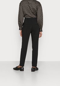 Svarta skräddarsydda byxor med smal passform, som har två bakfickor, bärs med en mönstrad långärmad skjorta och svarta fin skor.