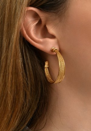 Boucles d'oreilles en or en forme de créole avec une surface texturée, dotées d'un accent enroulé sur le dessus et d'une forme élégante et courbée.