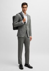 Gray wool blend suit with a tailored fit, featuring a notch lapel jacket, matching trousers, and black leather shoes. Black backpack on shoulder.