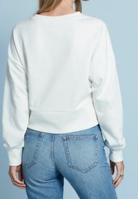 Sweatshirt blanc à coupe décontractée, col et poignets côtelés, associé à un jean taille haute bleu clair. Texture lisse et design décontracté.