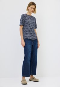 Camiseta gris con estampado, de manga corta y cuello redondo, combinada con unos vaqueros de pierna ancha azul oscuro y unos zuecos beige de tipo slip-on.