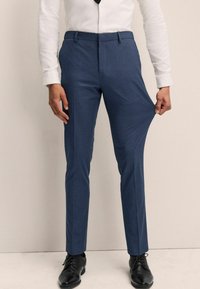 Blaue maßgeschneiderte Hosen aus glattem Stoff; schmale Passform mit Seitentaschen, getragen mit einem weißen Hemd und schwarzen Schuhen, was einen formellen Stil zeigt.