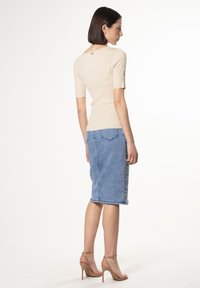 Maglietta a maglia beige chiaro con maniche corte, abbinata a una gonna a tubino in denim di lavaggio medio. Presenta un design aderente e una texture sottile.
