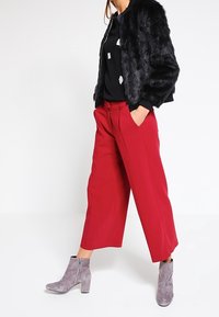 Svart syntetpälsjacka med beskuren design, matchad med vida röda byxor och grå ankelstövlar med sidodragkedja.